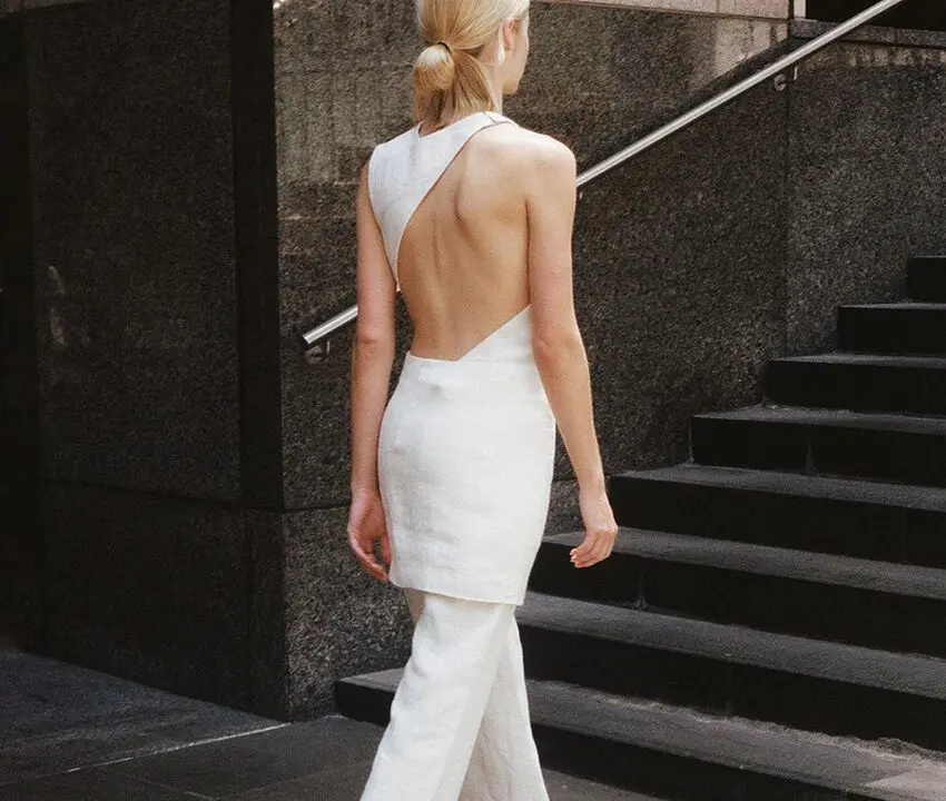 TN - A women facing backwards to the camera, wearing a white backless dress and climbing up the stairs